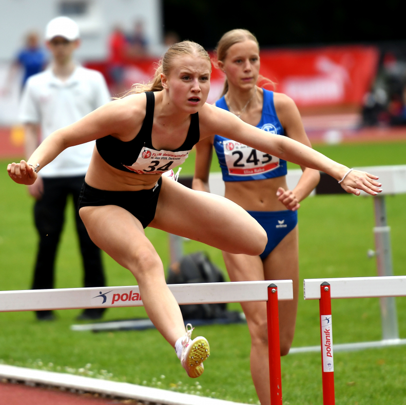Galavorstellung von Maja Bolinger: Die junge LAZ-Athletin glänzte über 100-Meter-Hürden in einem tollen Finale mit Platz zwei und ist mit 14,13 Sekunden aktuell die fünftbeste Deutsche des jüngeren U18-Jahrgangs. Foto: Bottin|Überraschende Vizemeisterschaft: Multitalent Nia Ferige (rechts) vom LAZ Soest - hier im Zweikampf mit der Paderbornerin Ida Pauline Göke - verbesserte sich über 80-Meter-Hürden bei der W15 deutlich auf starke 12,60 Sekunden. Foto: Bottin|LAZ-Sprinterin Maja Bolinger bewies auch im Weitsprung mit neuer persönlicher Bestleistung von 5,32 Metern und Platz vier bei der weibl. Jugend U18  ihre Qualitäten. Foto: Bottin|Viel Sand um Nichts? Keineswegs. Sprinttalent Maja Bolinger vom LAZ Soest überzeugte bei den Westfalenmeisterschaften in Dortmund neben ihrer neuen Hürdenbestzeit auch im Weitsprung mit 5,32 Metern und Platz vier. Foto: Bottin|Mit Maja Bolinger freute sich auch das Maskotchen von Ausrichter LG Olympia Dortmund über die tollen Leistungen der Athletin vom LAZ Soest bei den &quot;Westfälischen&quot;. Foto: Bottin|Strahlende Westfalenmeisterin: Laura Voß (Mitte) vom LAZ Soest siegte über 400-Meter-Hürden in persönlicher Bestzeit und ließ Chantal Maschinski (links, Hamm)) und Anne Schwedler (Bochum) um Längen hinter sich. Foto: Bottin|||